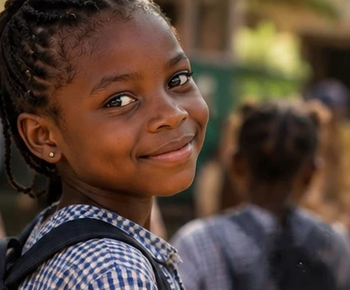 Une écolière souriante, cartable sur le dos, devant son école